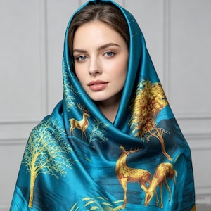 May include: A teal silk scarf with a landscape design featuring golden deer and trees. The scarf is draped over the head and shoulders, creating a hooded effect. The design includes a mountain range and a blue background.