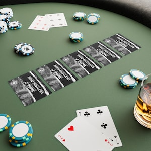 May include: A poker game setup on a green felt table. Playing cards and poker chips are scattered around. Several playing cards are face up, and a glass of amber liquid is visible. The cards have the text "HARU HUSTLERS J-KUME".