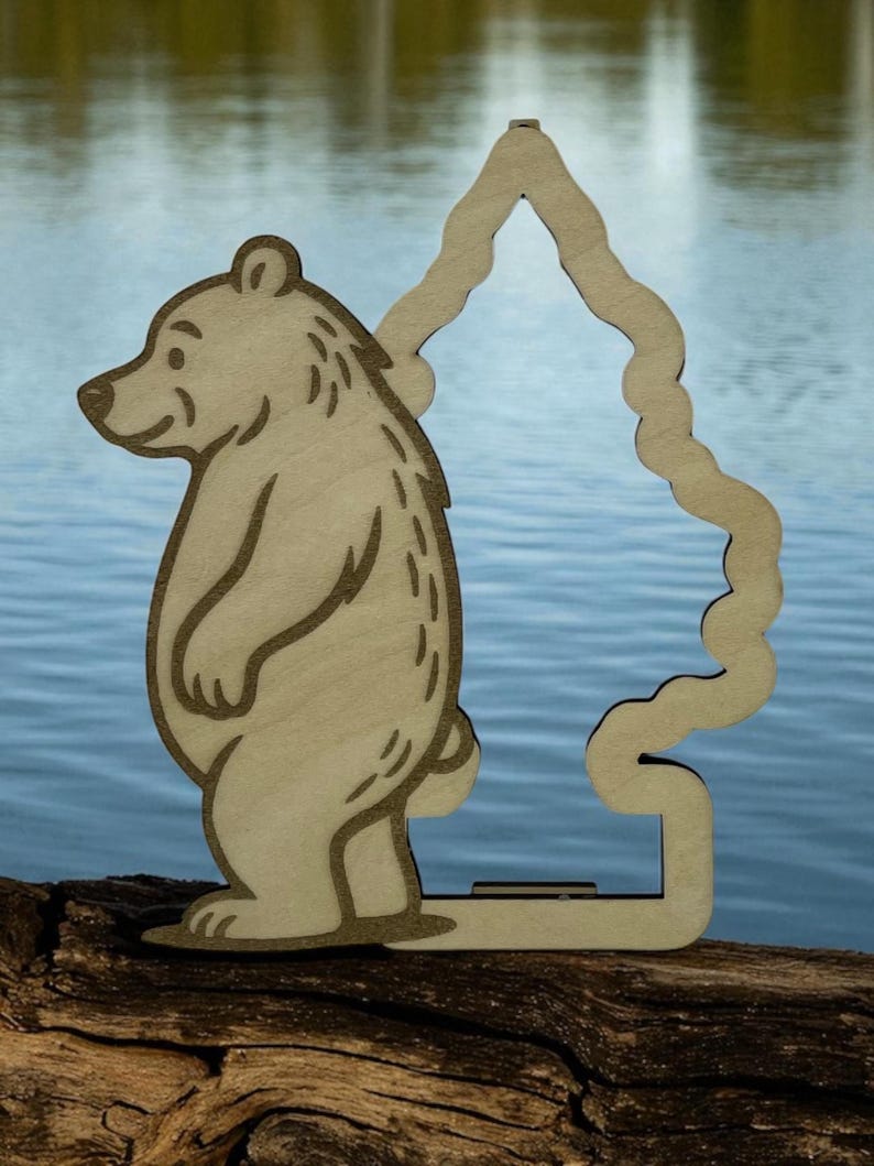 May include: A light brown wooden bear figure with a tree-shaped cutout. The bear has etched details and stands on a wooden base. The background shows a body of water.