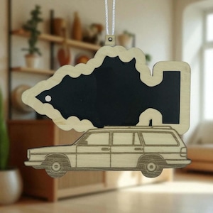 May include: Wooden Christmas ornament featuring a station wagon design. The ornament has a black chalkboard area in the shape of a Christmas tree. The ornament is made of light-colored wood and has a white string for hanging.