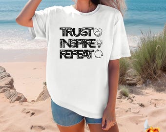 Peut inclure: T-shirt blanc avec le texte "TRUST INSPIRE REPEAT" en lettres noires. Le texte est stylisé avec un cœur, une ampoule et une flèche circulaire.