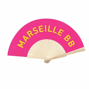 Peut inclure: Éventail rose vif avec l'inscription jaune "MARSEILLE BB". Le manche est en bois et le design est en papier plissé. Le texte "LE BAZAR MARSEILLAIS" est imprimé sur le manche.
