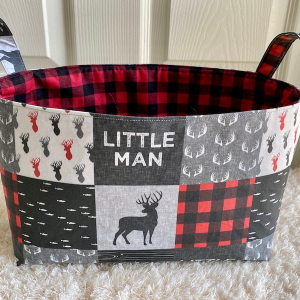 May include: A gray and red fabric storage basket with handles. The basket is decorated with a patchwork design featuring deer, antlers, and the words "Little Man".