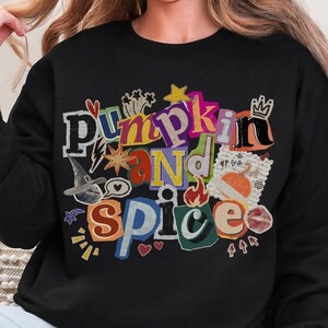 Peut inclure: Sweat-shirt noir avec l'inscription "Pumpkin and Spice" dans un style collage coloré. Le motif comprend un chapeau de sorcière, des cœurs et une étoile. Le sweat-shirt est de style col rond.