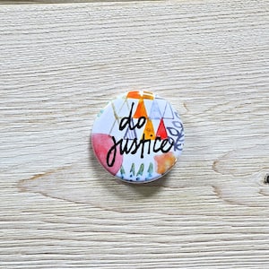 May include: A round button with a white background and colorful geometric shapes. The text "do justice" is written in black cursive lettering.