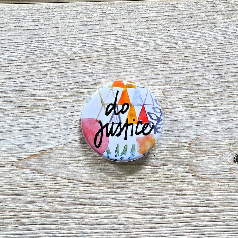 May include: A round button with a white background and colorful geometric shapes. The text "do justice" is written in black cursive lettering.