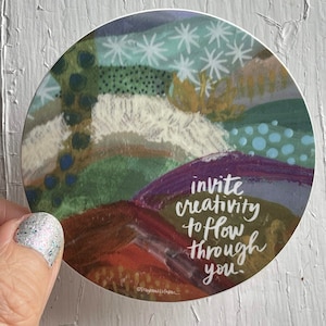 May include: A round sticker with an abstract painting of colorful shapes and textures. The text "invite creativity to flow through you" is written in white on the sticker.