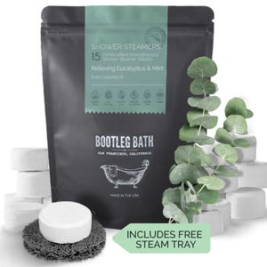 May include: A black pouch with a white label that reads "Shower Steamers 15 Handcrafted Aromatherapy Shower Steamer Tablets Relieving Eucalyptus & Mint Pure Essential Oil" and "Bootleg Bath San Francisco, California Made in the USA". The pouch is next to a stack of white shower steamer tablets and a sprig of eucalyptus.