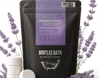 May include: A black bag of "Shower Steamers" with "Calming Lavender Mint" text, 15 tablets, and a "Made in USA" sticker. The bag is next to a stack of white tablets and sprigs of lavender.