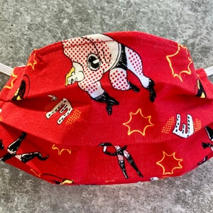 May include: Red face mask with a repeated pattern of black and white cartoon figures in superhero poses. The background is red with yellow stars.