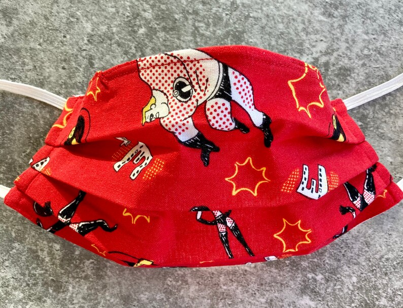 May include: Red face mask with a repeated pattern of black and white cartoon figures in superhero poses. The background is red with yellow stars.