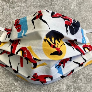 May include: A white face mask with a repeating pattern of a superhero in red, yellow, and black. The superhero is in various poses, including flying and punching.