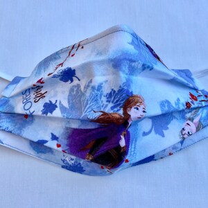 May include: A blue and white face mask with a Frozen theme. The mask features Anna and Elsa from the movie Frozen. The text "FOREST SPIRITS" is printed on the mask.
