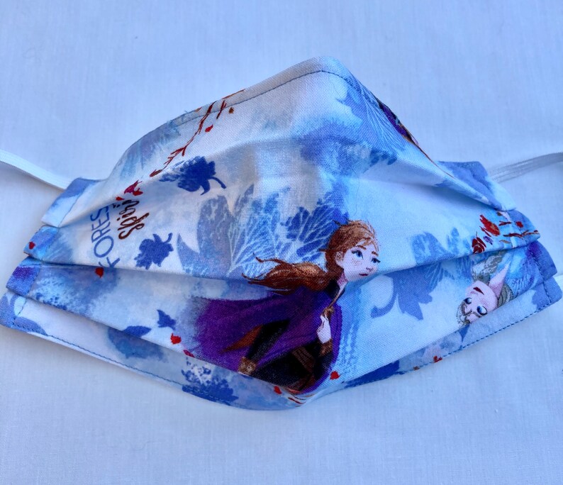 May include: A blue and white face mask with a Frozen theme. The mask features Anna and Elsa from the movie Frozen. The text "FOREST SPIRITS" is printed on the mask.