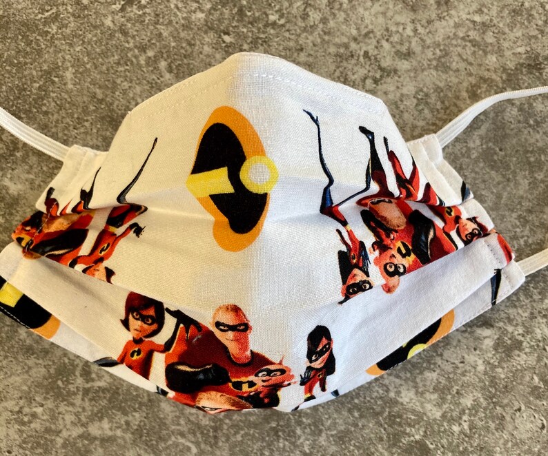 May include: White face mask with a colorful print of the Incredibles family. The mask has a white background with the Incredibles family in their superhero costumes. The mask also has a black and yellow symbol of Mr. Incredible's mask.
