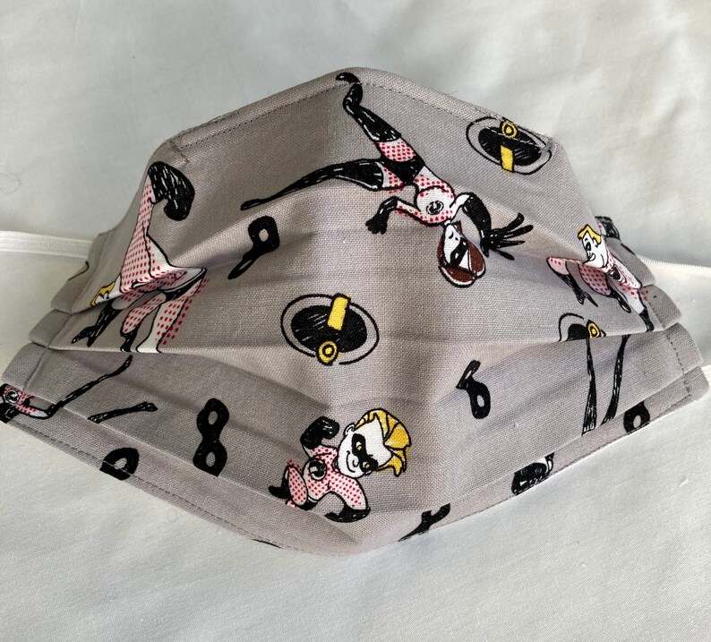 May include: Gray fabric face mask with a repeating pattern of cartoon characters from the Incredibles movie. The characters include Mr. Incredible, Elastigirl, Violet, and Dash.