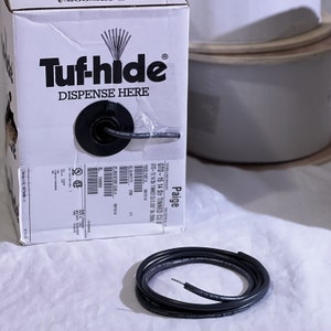 May include: A white box with the text "Tuf-hide" and "DISPENSE HERE" printed on it. The box contains a roll of black electrical wire. The label on the box reads "GTO-15 14 Str TINNED CU 0" and "GTO-15 14 Str TINNED CU 0.265 B 2508".