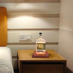 May include: A clear glass bottle with a label that reads "Knob Creek Rye" sits on a wooden base. The bottle is illuminated from within, creating a warm glow.
