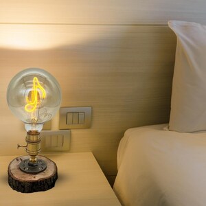 May include: A bedside table lamp with a wooden base and a clear glass bulb with a musical note filament. The lamp is turned on and the filament is glowing.