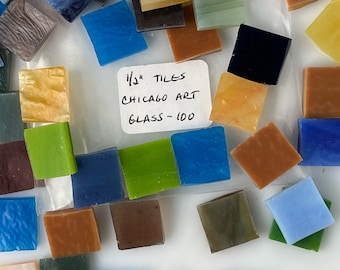May include: A collection of 100 1/2 inch glass tiles in various colors, including blue, green, yellow, brown, and orange. The tiles are arranged on a white surface with a label that reads "1/2" Tiles Chicago Art Glass - 100".