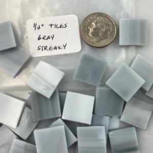 May include: A bag of 1/2 inch gray streaky glass tiles. The tiles are square and have a light gray color with darker gray streaks. A US dime is included for scale.
