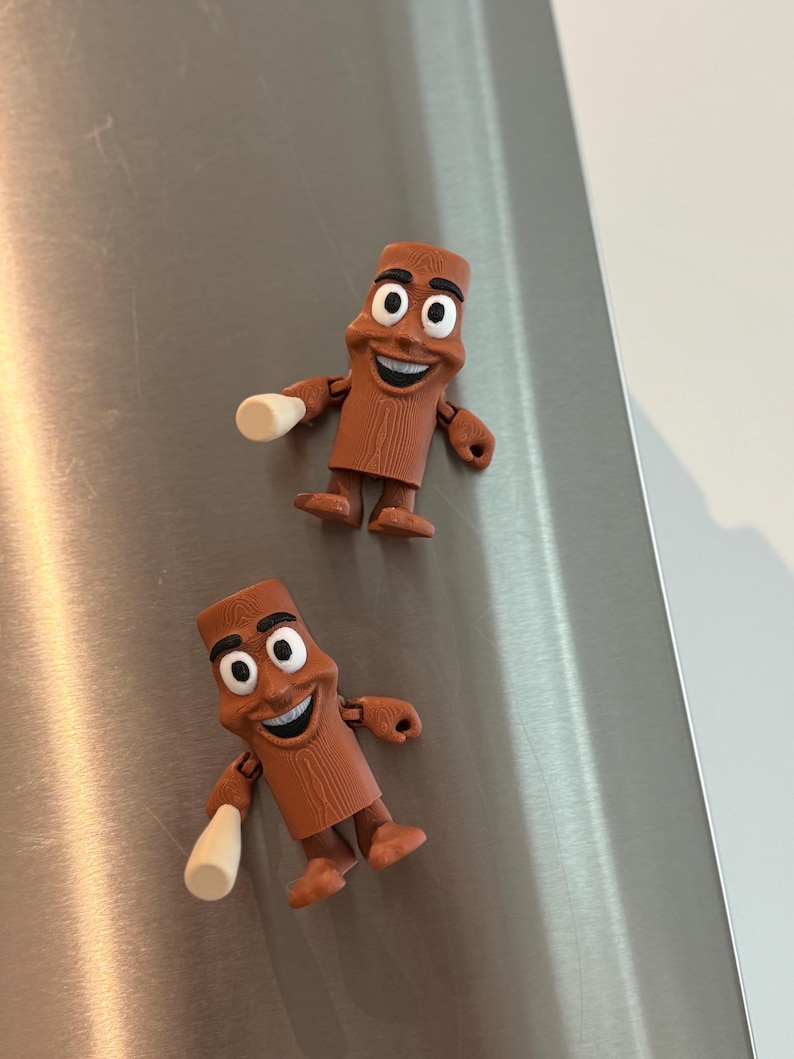 May include: Two brown, cartoon-like figures with smiling faces and white cylindrical objects in their hands. The figures have black eyes and are posed as if they are waving. They are set against a brushed metal background.