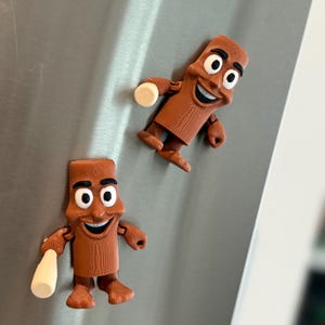 May include: Two brown, cartoon-like magnets shaped like a smiling figure with a bottle. The magnets have a wood-grain texture and white eyes. One magnet holds a white bottle. The magnets are attached to a silver surface.