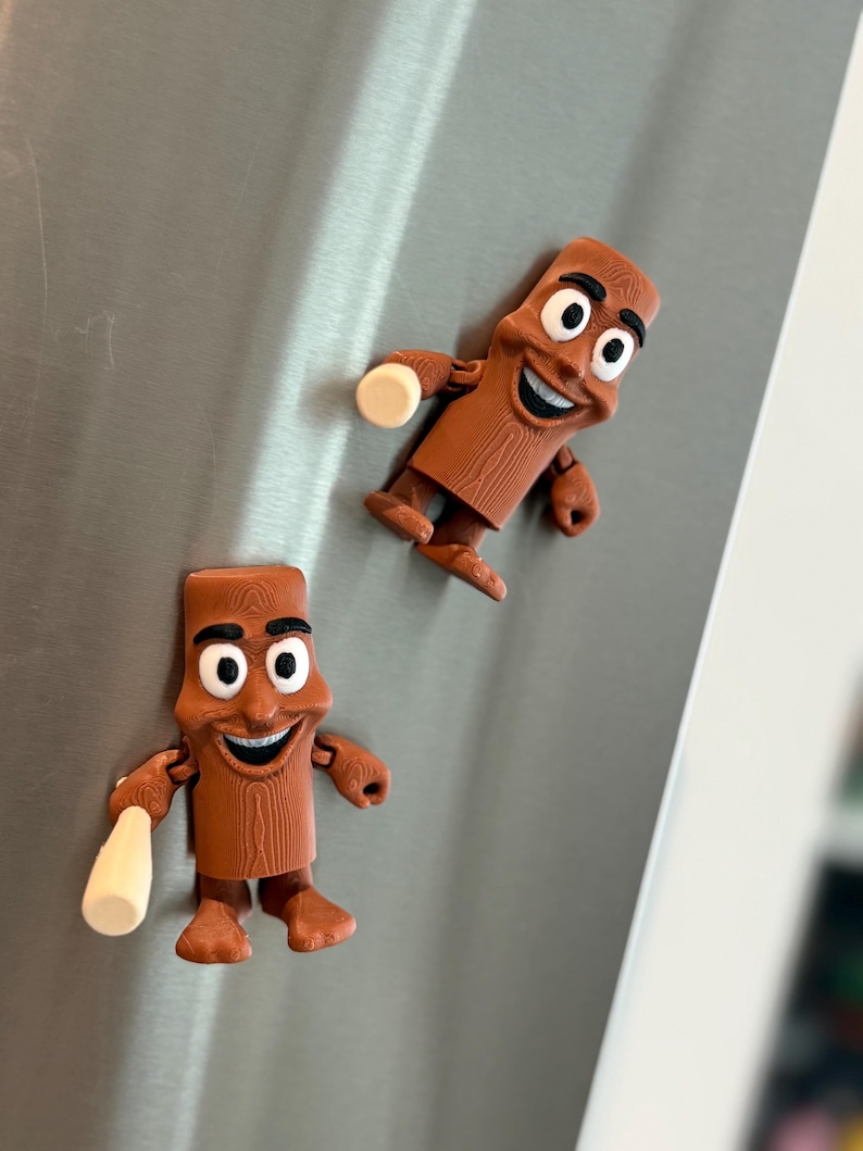 May include: Two brown, cartoon-like magnets shaped like a smiling figure with a bottle. The magnets have a wood-grain texture and white eyes. One magnet holds a white bottle. The magnets are attached to a silver surface.