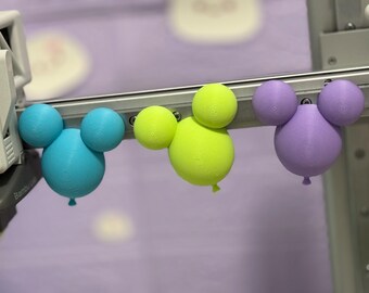 May include: Three 3D-printed balloon-shaped ornaments featuring a central sphere with two smaller spherical ears attached to the top. The ornaments are colored in bright cyan, neon yellow, and light purple, each with a small nozzle at the bottom.