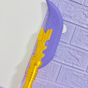 May include: A decorative prop weapon with a purple blade and gold accents. The blade has intricate designs, and the handle is gold with a ribbed texture. The weapon is set against a purple brick wall.
