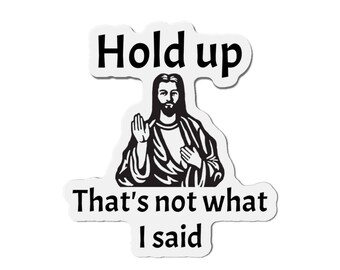 May include: A white sticker featuring a black and white illustration of Jesus with the text "Hold up" above and "That's not what I said" below. The text is in black.