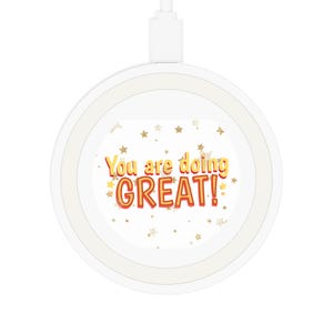 Könnte beinhalten: Ein weißes kabelloses Ladegerät mit einer goldenen und roten Grafik, auf der "You are doing GREAT!" mit goldenen Sternen auf weißem Hintergrund steht.