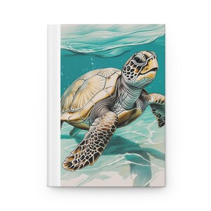 May include: A white hardcover journal featuring a detailed illustration of a sea turtle swimming underwater. The turtle has a tan shell with dark brown markings, and the water is a vibrant turquoise color.