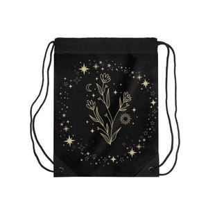 Peut inclure: Sac de sport noir avec un motif floral doré, des étoiles, un croissant de lune et un soleil. Le motif est entouré d'un cercle d'étoiles. Le sac a des cordons noirs.