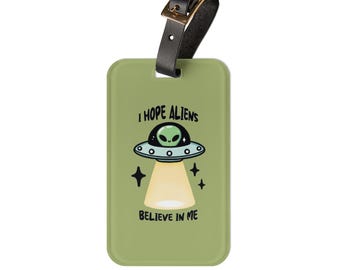 May include: Green luggage tag with a black strap and a cartoon image of a UFO with an alien inside. The text on the tag reads "I hope aliens believe in me."