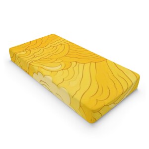 Könnte beinhalten: Ein gelbes Spannbettlaken für ein Babybett mit einem welligen, abstrakten Muster.