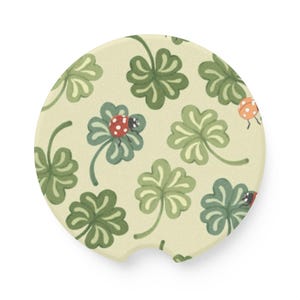 May include: A round, beige coaster with a green four-leaf clover pattern and red and orange ladybugs.