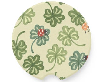 May include: A round, beige coaster with a green four-leaf clover pattern and red and orange ladybugs.