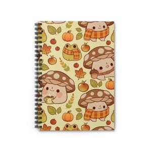 May include: A spiral bound notebook with a yellow background and a repeating pattern of mushrooms, frogs, and autumn leaves. The mushrooms are wearing scarves and holding cups of tea. The frogs are wearing scarves and holding acorns.