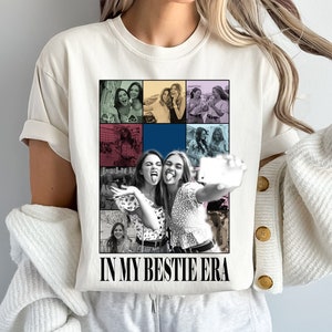 May include: White t-shirt featuring a collage of photos of two women smiling and taking a selfie. The text "In My Bestie Era" is printed on the shirt.