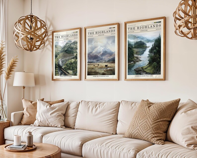 May include: Three framed landscape prints titled "The Highlands" hang above a beige sofa. The prints feature scenic views of mountains, a bridge, and a river. The frames are a light brown colour, and the prints have a vintage newspaper aesthetic.