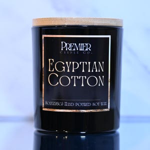 May include: A black candle jar with a wooden lid. The label reads "Premier Candle Co. Egyptian Cotton 8oz (226g) Hand Poured Soy Wax".