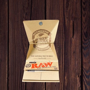 Peut inclure: Un paquet de feuilles &agrave; rouler RAW Classic de taille 1 1/4. Le paquet est en carton brun et porte une &eacute;tiquette blanche avec le logo RAW et le texte "Natural Unrefined Rolling Papers".