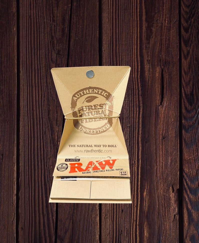 Peut inclure: Un paquet de feuilles &agrave; rouler RAW Classic de taille 1 1/4. Le paquet est en carton brun et porte une &eacute;tiquette blanche avec le logo RAW et le texte "Natural Unrefined Rolling Papers".