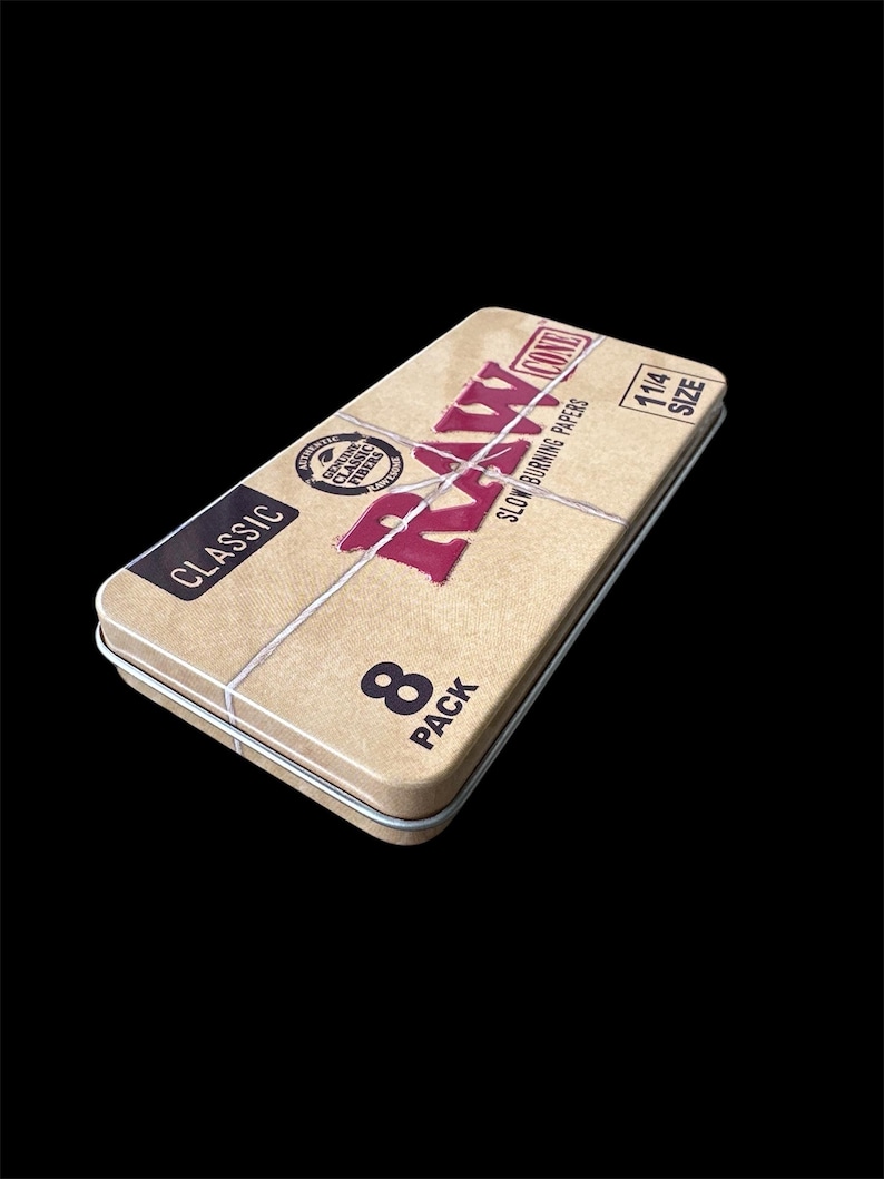 May include: A rectangular, tan metal tin with the word "RAW" in red, and the word "CLASSIC" in black. The tin also has the text "SLOW BURNING PAPERS" and "8 PACK". The tin is 114 size.