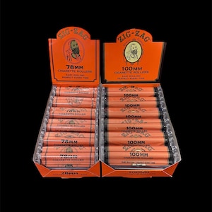 May include: Two boxes of Zig-Zag cigarette rollers, one box of 78mm rollers and one box of 100mm rollers. The boxes are orange and feature a bearded man's face with the Zig-Zag logo.