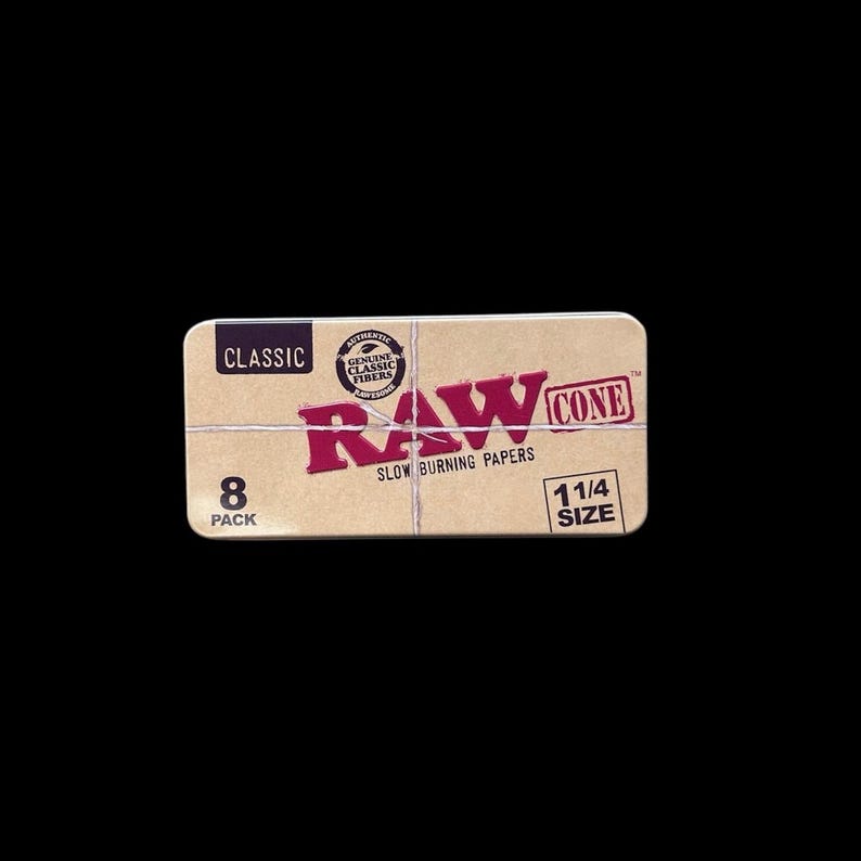 May include: A rectangular box of RAW Cone slow-burning papers. The box is tan with red text that reads "RAW CONE" and "SLOW BURNING PAPERS." It also has the text "8 PACK" and "1 1/4 SIZE."