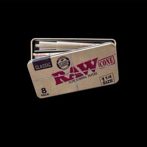 May include: A tan metal tin with the word "RAW" in red, and the text "CONE 1 1/4 SIZE" in white. The tin is open, revealing pre-rolled cones. The text "CLASSIC" and "8 PACK" are also visible. The product is designed for slow burning.