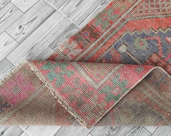 May include: A folded vintage rug with a pink, green, and blue pattern. The rug has a fringe border and is made of woven fabric.