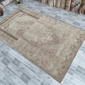 May include: A beige prayer rug with a brown floral pattern and a central design. The rug has a worn, vintage look.